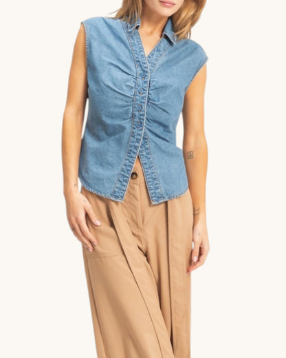 Woman wearing a denim sleeveless shirt with beige pants on a white background