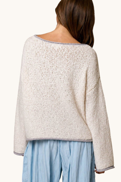 A woman shown from the back wearing a loose, textured knit sweater in a light cream or off-white color, paired with light blue pants, against a plain light background.