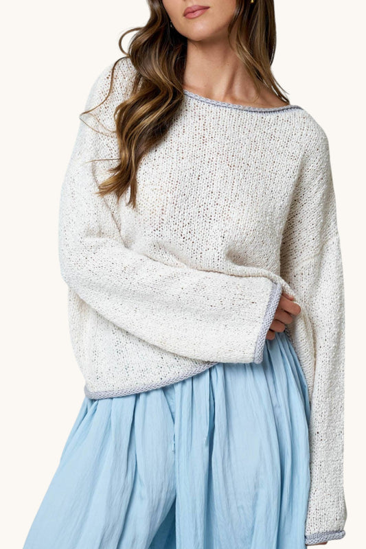A woman wearing a chunky knit off-white sweater with a light grey trim and a light blue skirt, shown from the neck down against a plain light background.