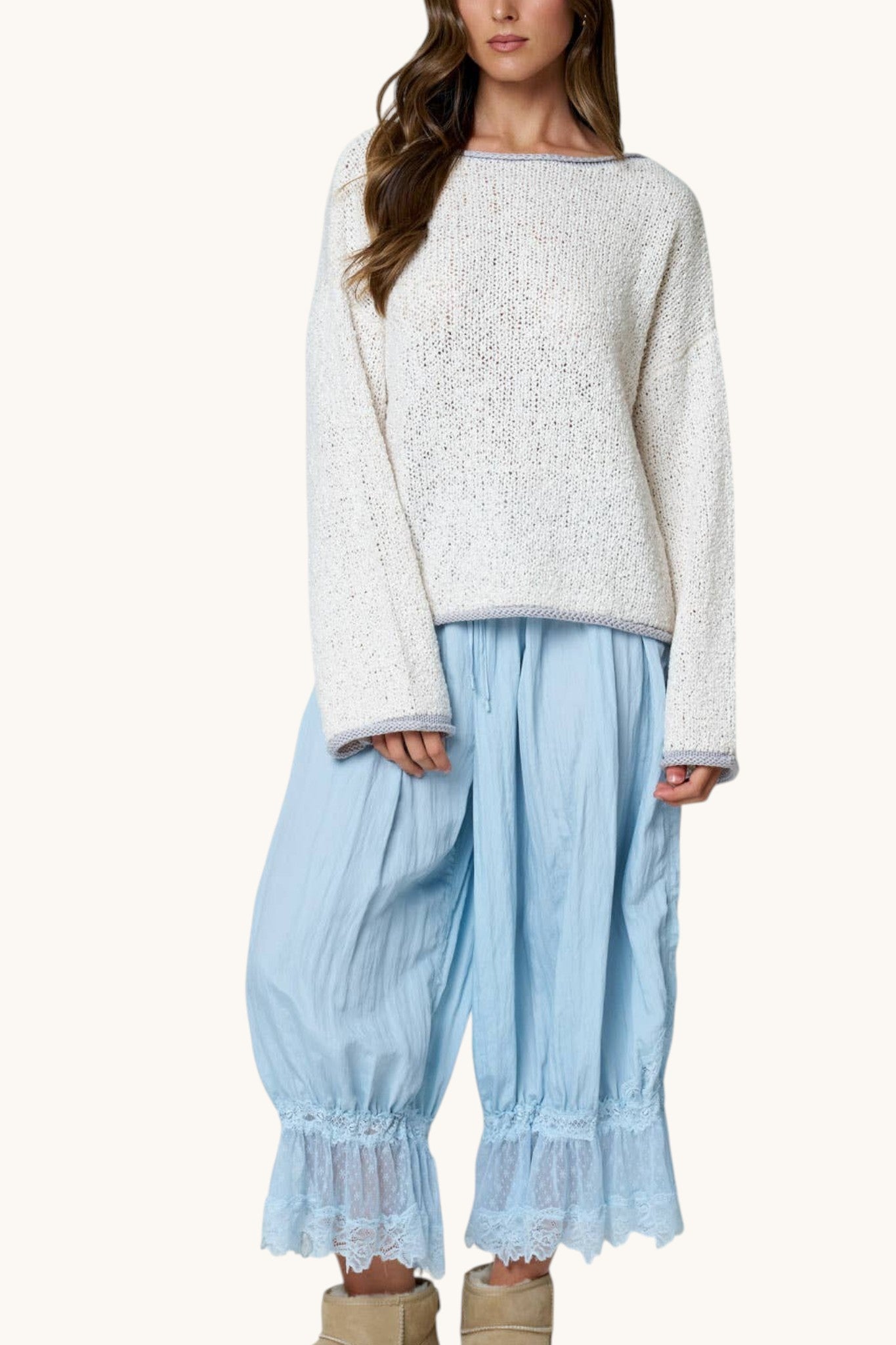 A woman modeling a light cream textured knit sweater and light blue wide-leg pants with ruffled hems, shown against a plain off-white studio background.