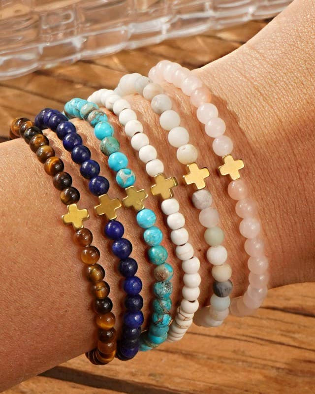 Close-up of a wrist wearing multiple beaded bracelets with crosses on a wooden surface.