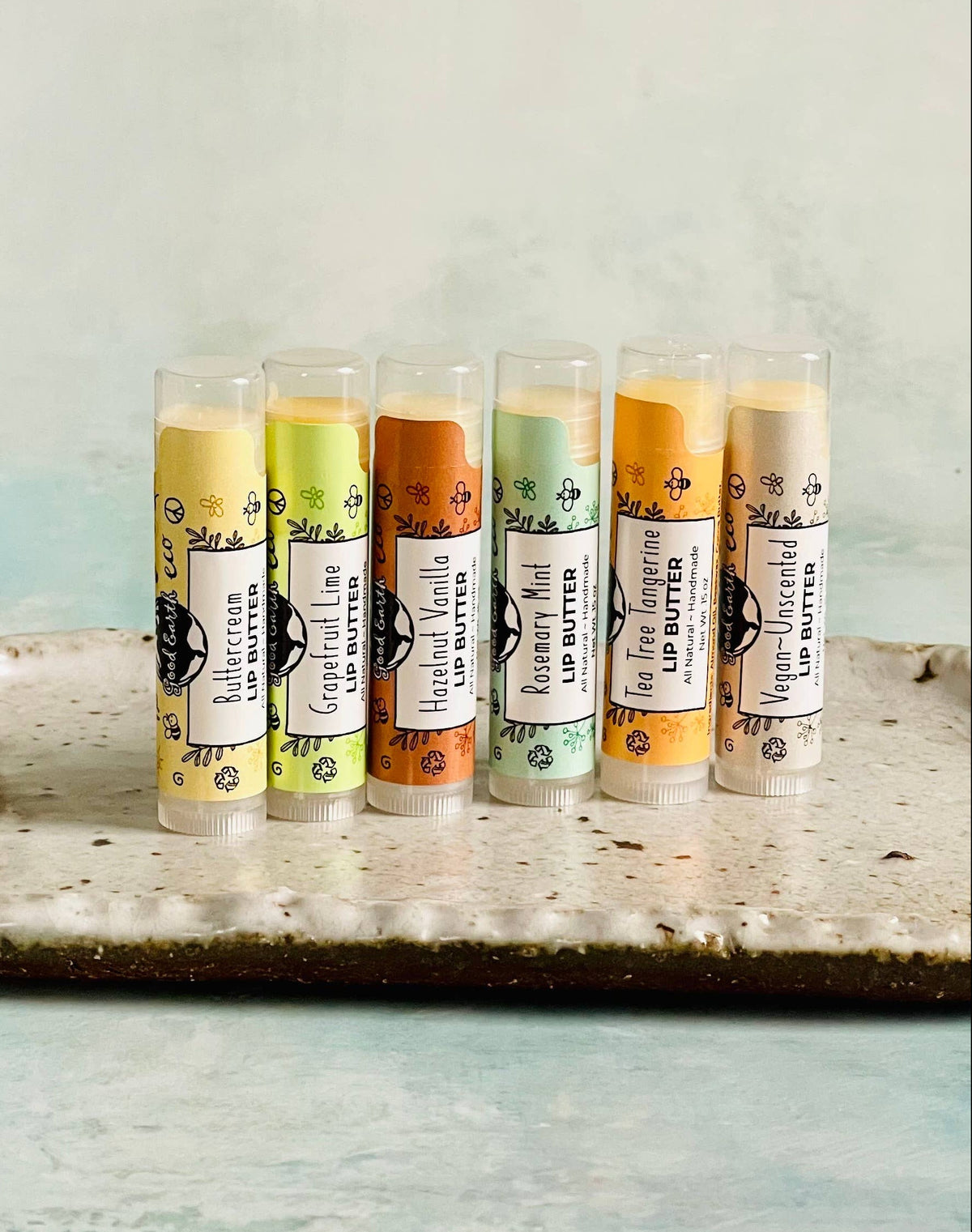 6 lip balms in different flavors lined up on stone plate on neutral background.