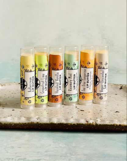 6 lip balms in different flavors lined up on stone plate on neutral background.