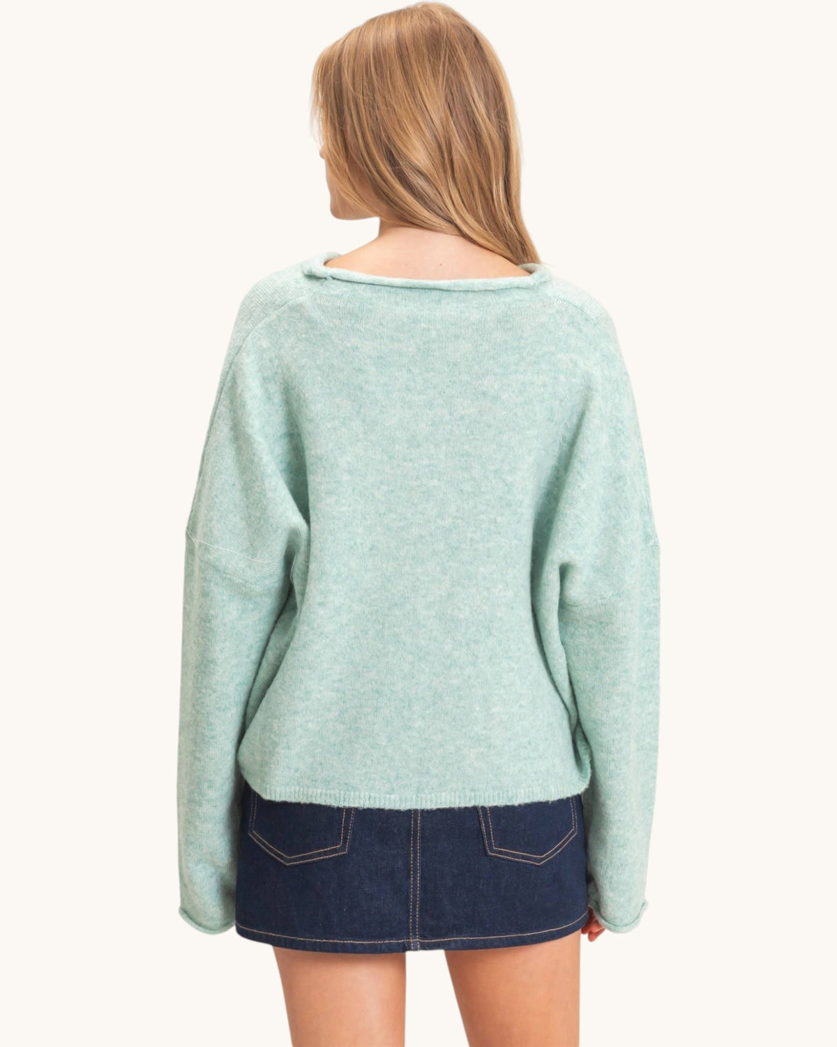 A woman shown from the back wearing a light mint green knit sweater and a dark denim mini skirt against a plain off-white background.