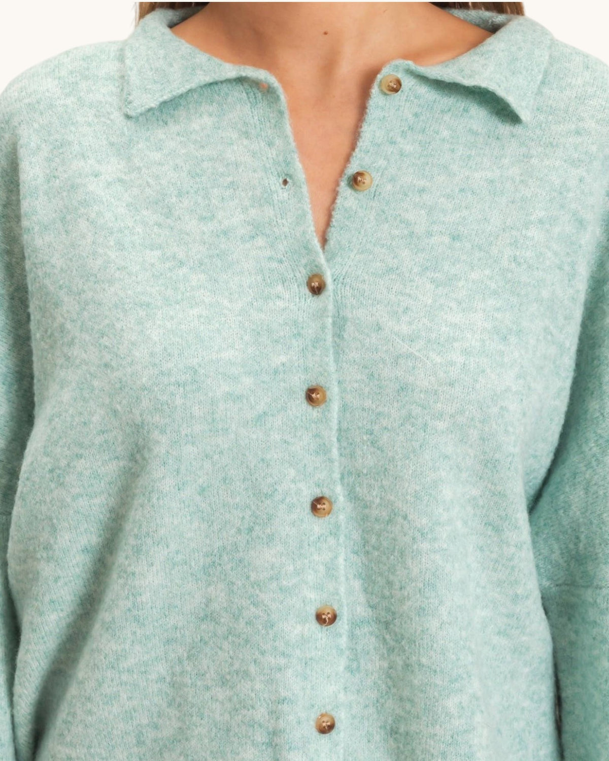 A close-up of a person wearing a light mint green knit polo cardigan with brown buttons.