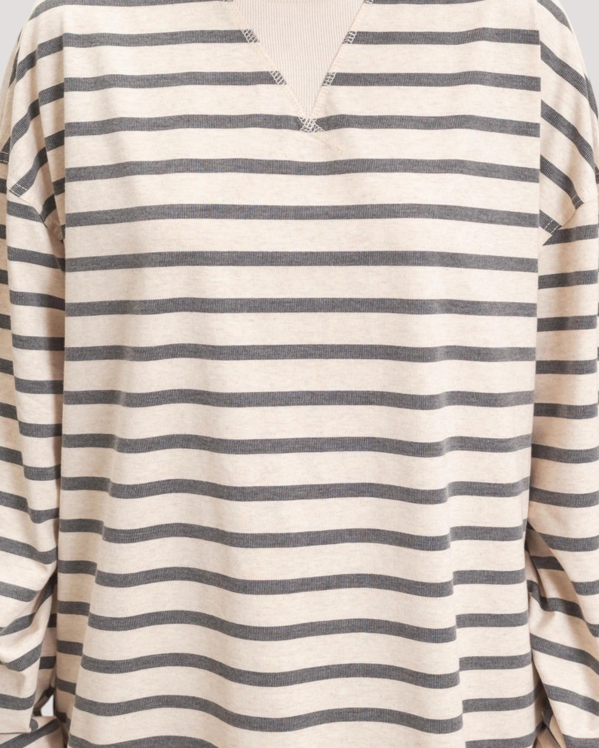 A close-up of a long-sleeve knit top with horizontal stripes in dark gray on a warm off-white or cream base. The neckline features a split V-cut with small decorative stitched details at the tips.