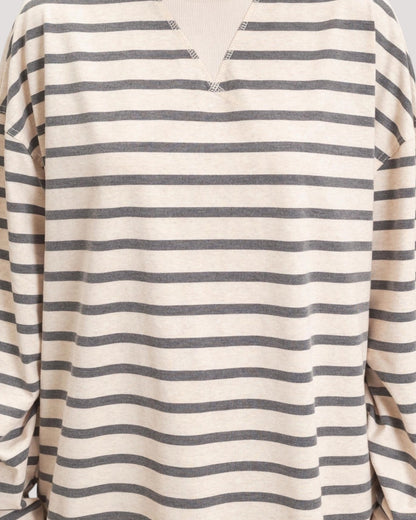 A close-up of a long-sleeve knit top with horizontal stripes in dark gray on a warm off-white or cream base. The neckline features a split V-cut with small decorative stitched details at the tips.