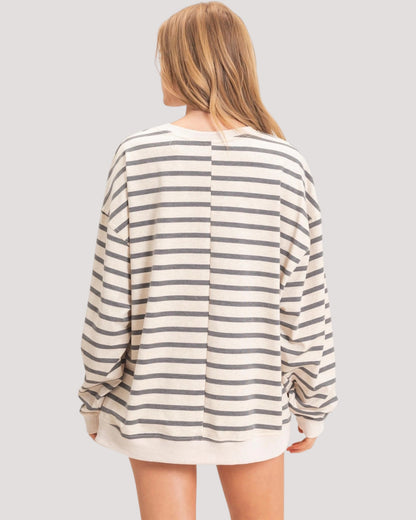 A woman shown from the back wearing an oversized long-sleeve striped top with horizontal beige and dark gray stripes, set against a solid light gray background.