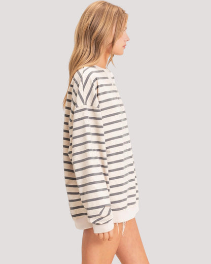 A woman shown from the side wearing a cream-colored sweatshirt with thin dark gray horizontal stripes, set against a solid light gray studio background.