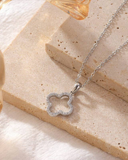 Silver necklace with a clover-shaped pendant on a beige surface.