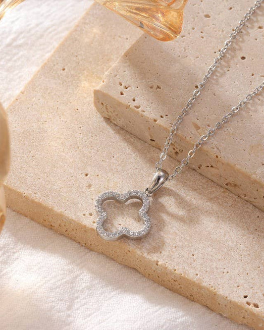 Silver necklace with a clover-shaped pendant on a beige surface.