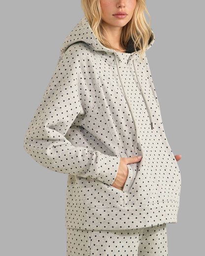 A woman wearing a light gray hooded sweatshirt and matching pants, both covered in a small black polka dot pattern, against a solid gray background.