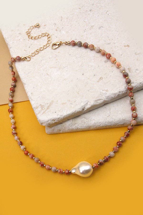 Necklace with beads and a pearl pendant on a textured surface.