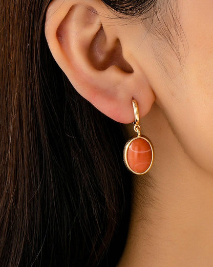 Close-up of an ear wearing a gold earring with a orange stone on a neutral background.