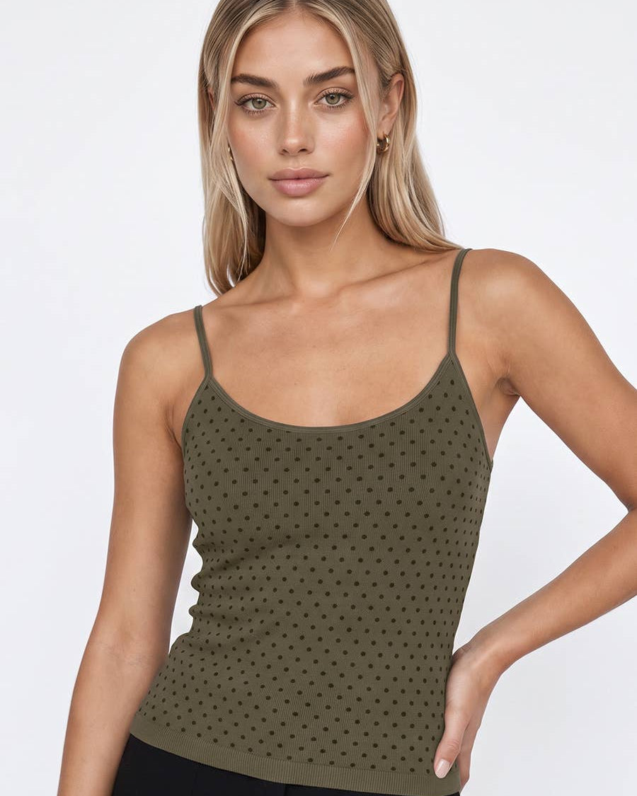 A woman modeling an olive green knit camisole top with a small repeating dot pattern, paired with black pants against a light gray studio background. 