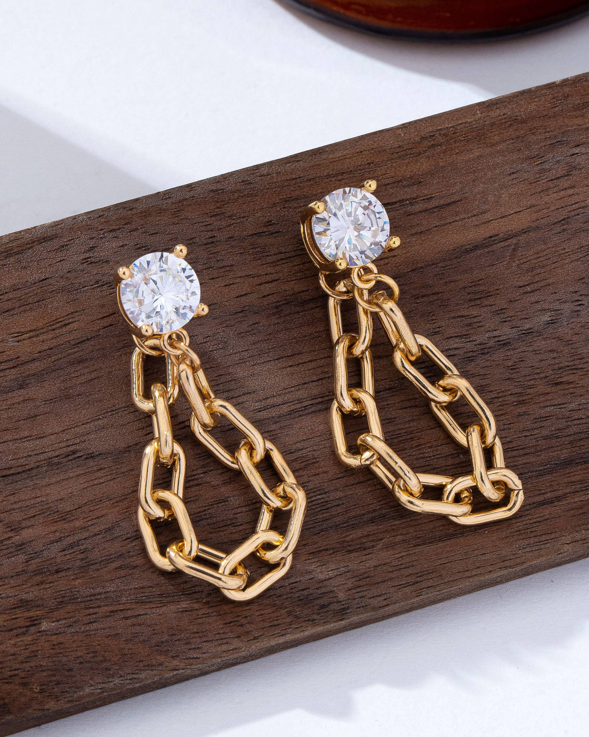 Gold chain earrings with clear gemstones crystal studs on a wooden surface.