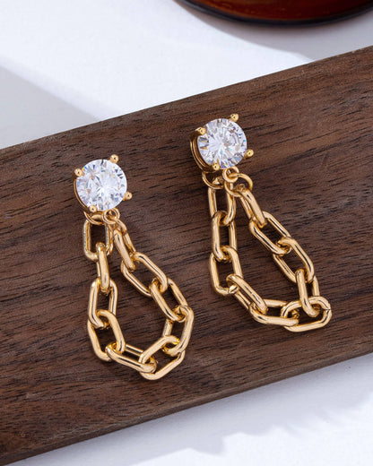 Gold chain earrings with clear gemstones crystal studs on a wooden surface.