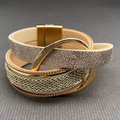 A multi-layered leather and metal cuff bracelet featuring a textured light beige leather band, a gold-tone chain link section, and polished gold-tone metal ring, displayed on a gray textured background.
