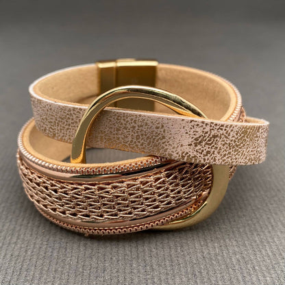 A close-up of a woven leather bracelet with a textured beige exterior, a metallic rose gold center band, and polished gold-toned hardware on a gray textured surface.
