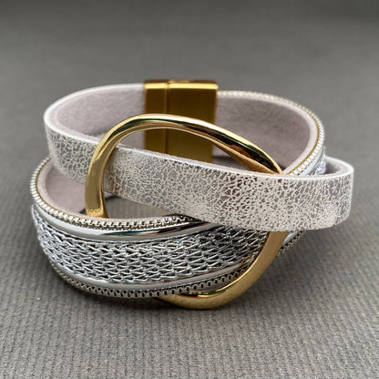 A multi-layered leather bracelet with textured silver layers, a woven silver center band, and polished gold-tone metal hardware, including a large ring and clasp, displayed on a gray textured background.
