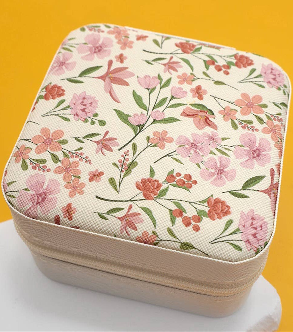 A square zippered case with a cream-colored fabric lid featuring a dusty rose, light pink and green floral pattern.