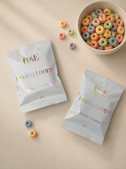 Two packets of 'Fruity Loops' shower steamers on a beige surface with colorful cereal loops.