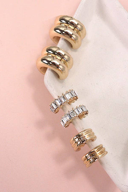 Set of gold huggie hoop earrings on a pink background.