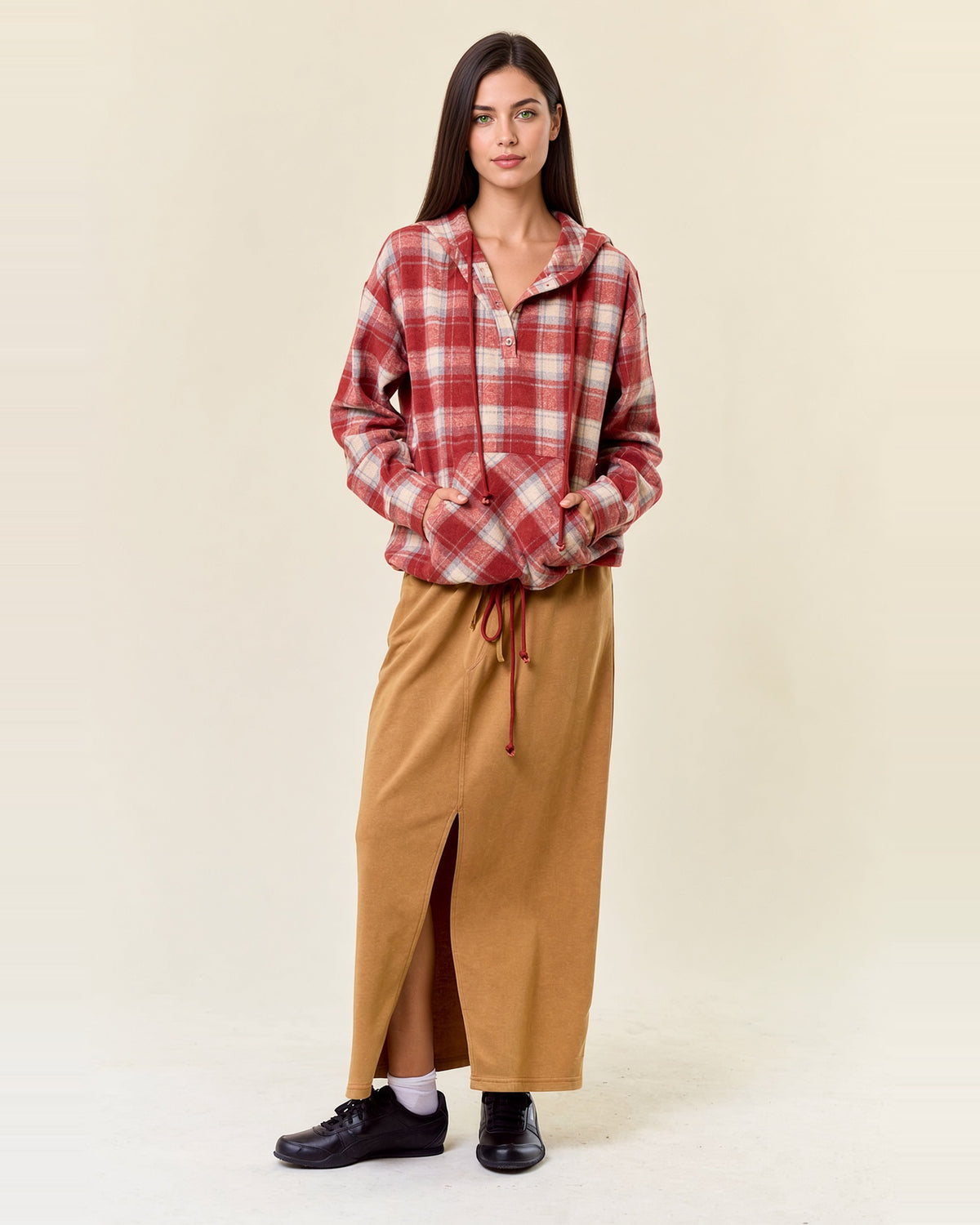 Full-length model wearing cranberry plaid flannel hoodie with hands in the kangaroo pocket and a tan skirt.