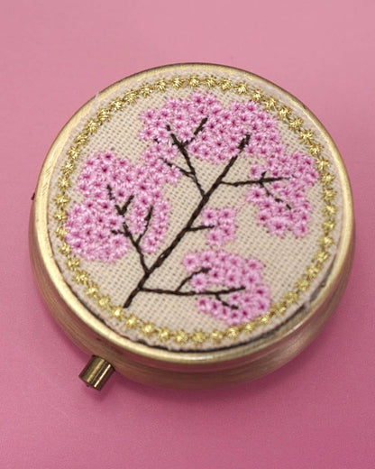 Embroidery pill case with cherry blossom design on a pink background.