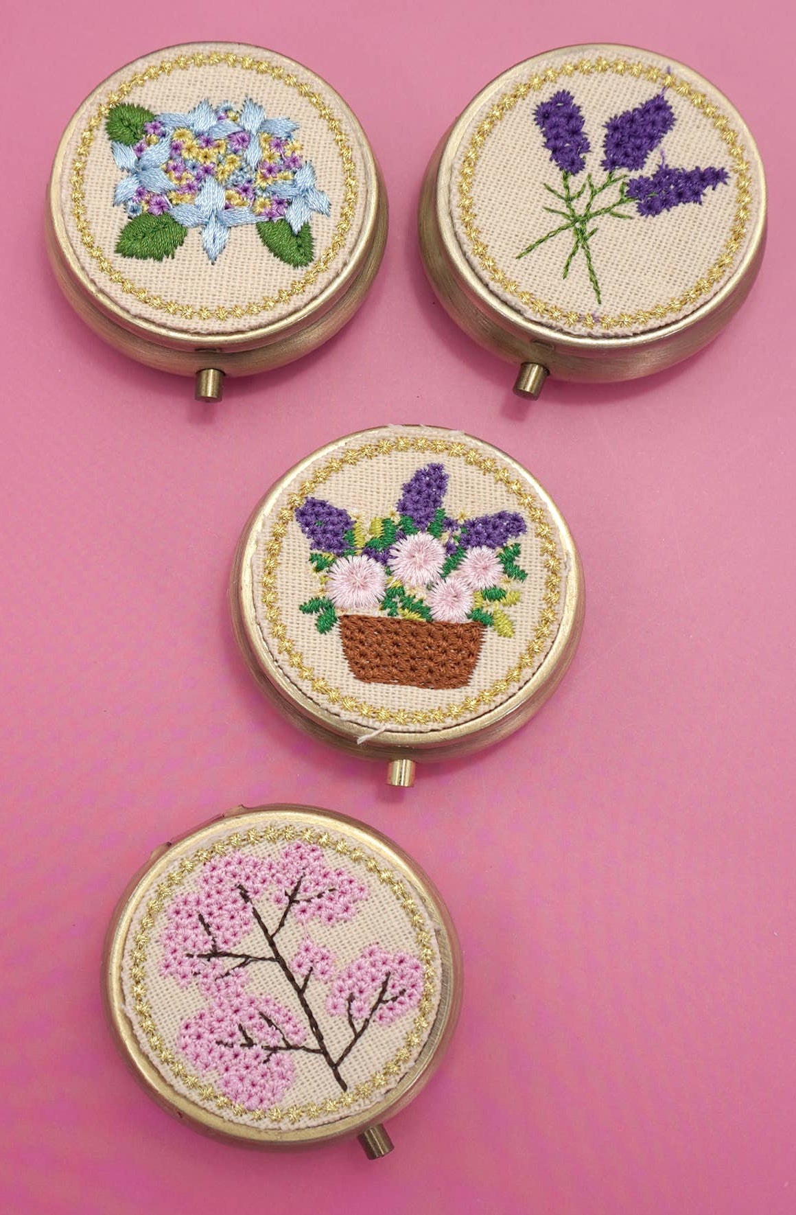 Four round floral embroidered and gold tone pill cases.