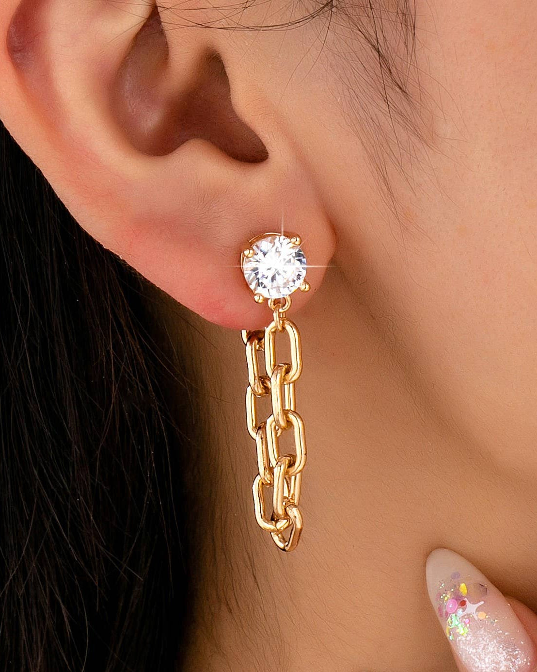 Gold chain earring with a round gemstone worn by a person.