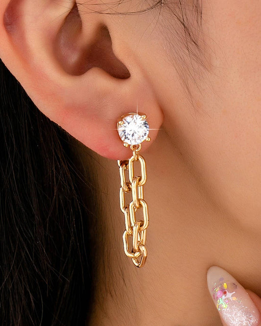 Gold chain earring with a round gemstone worn by a person.