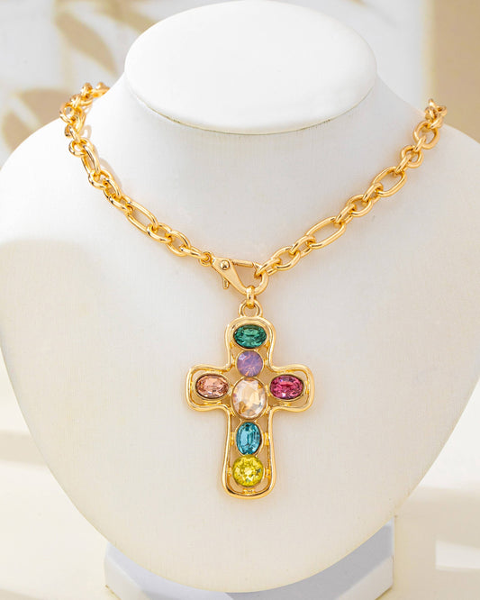 A gold cross pendant necklace with multiple colorful gemstones, displayed on a white jewelry bust.