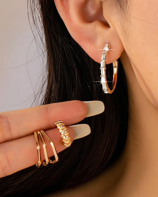 Close-up of a person wearing gold hoop earrings and holding additional gold crystal and geometric shaped hoops.