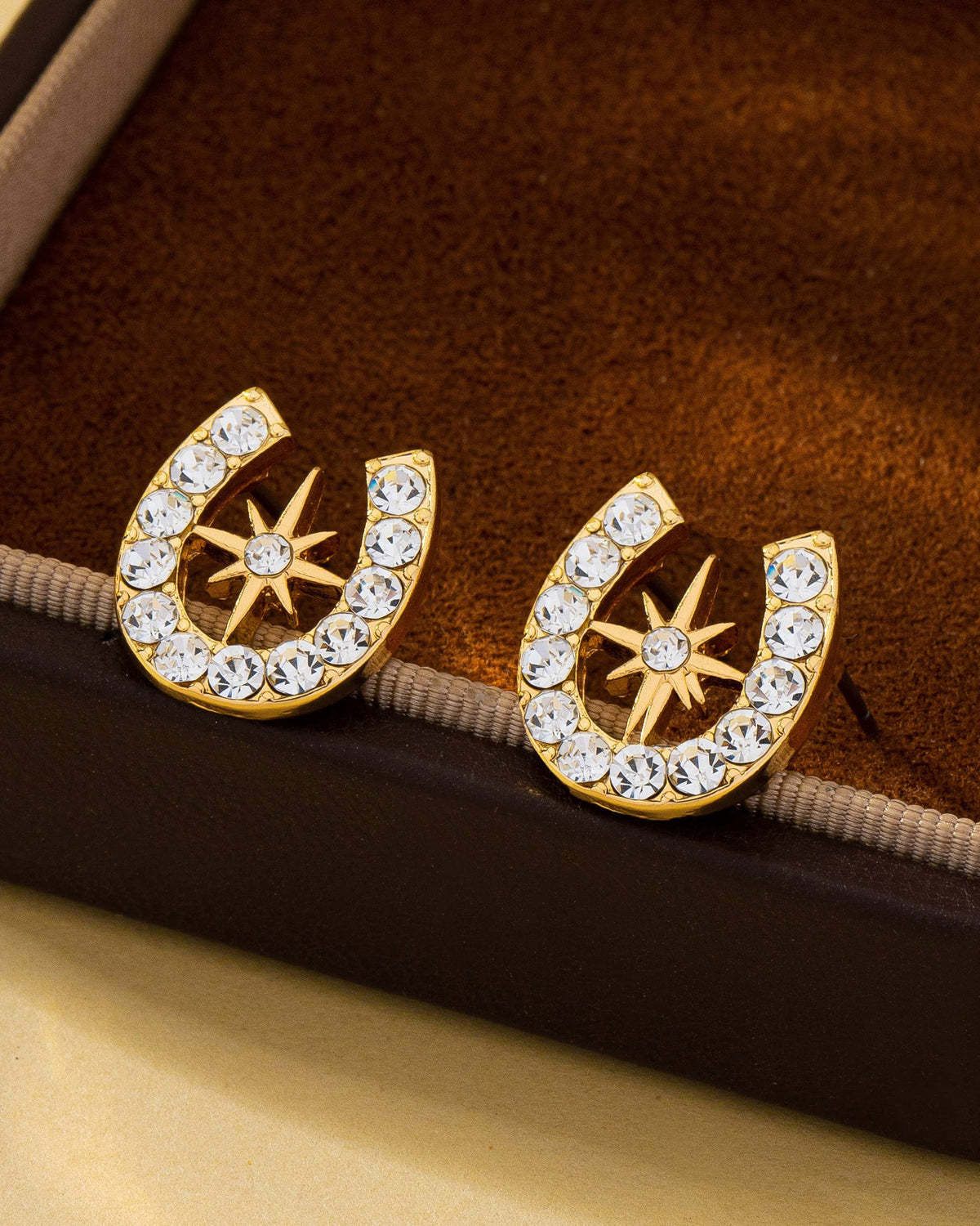 Gold horseshoe earrings with crystal star design on a brown velvet surface.