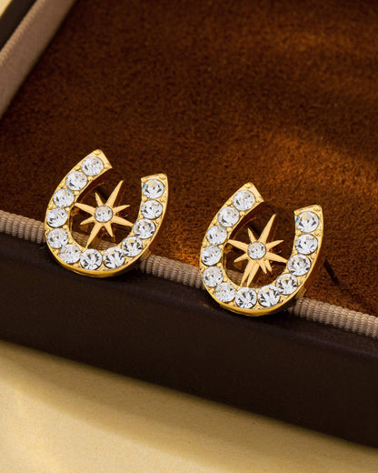 Gold horseshoe earrings with crystal star design on a brown velvet surface.