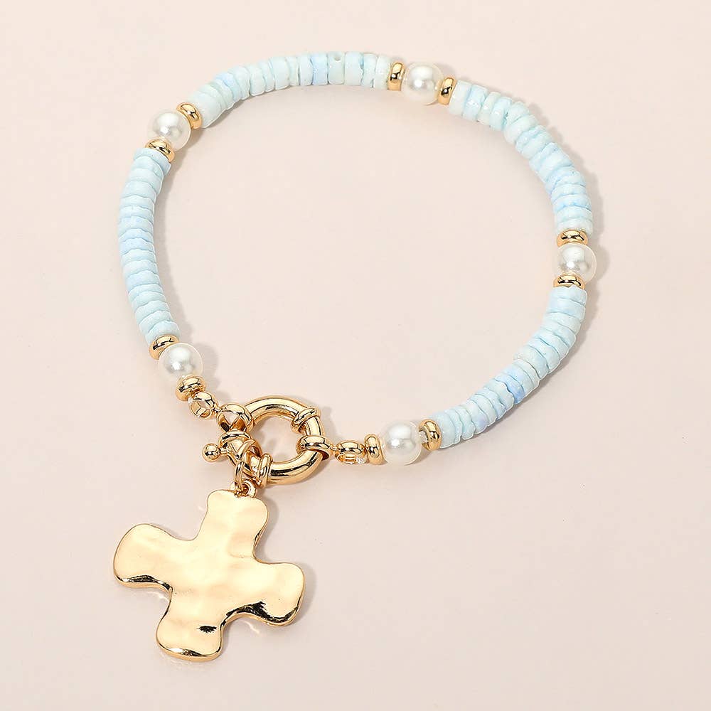 Bracelet with light blue beads, pearls, and a gold cross charm on a beige background.