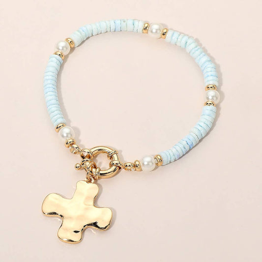 Bracelet with light blue beads, pearls, and a gold cross charm on a beige background.
