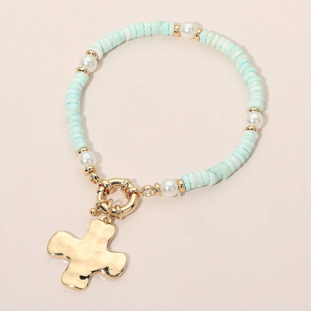 Bracelet with turquoise beads and a gold cross charm on a beige background.