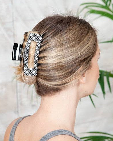 A woman shown from the back wearing a black and white plaid hair claw clip, holding her blonde hair in a low bun.