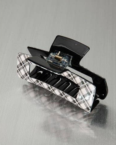 A black hair claw clip with a black-and-white plaid patterned outer frame, shown on a brushed gray metallic background.