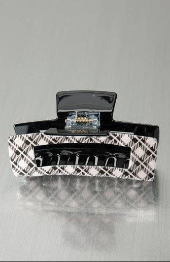 A black and white plaid patterned hair claw clip on a reflective gray surface.