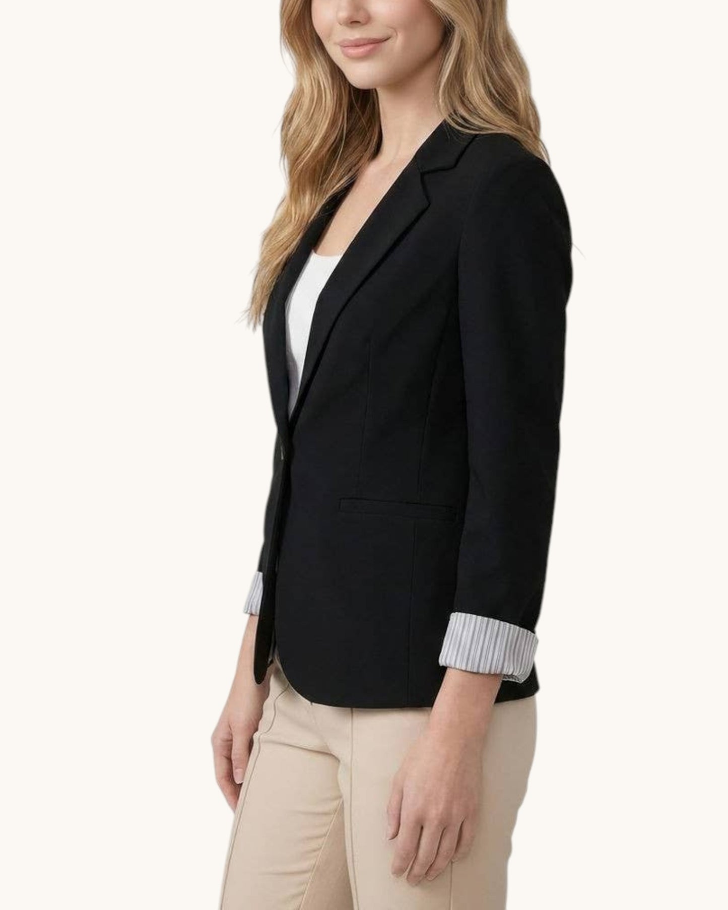 Woman wearing a black blazer over a white top with beige pants on a white background.