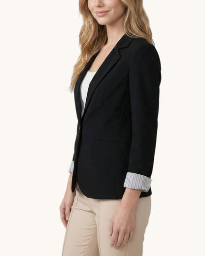 Woman wearing a black blazer over a white top with beige pants on a white background.