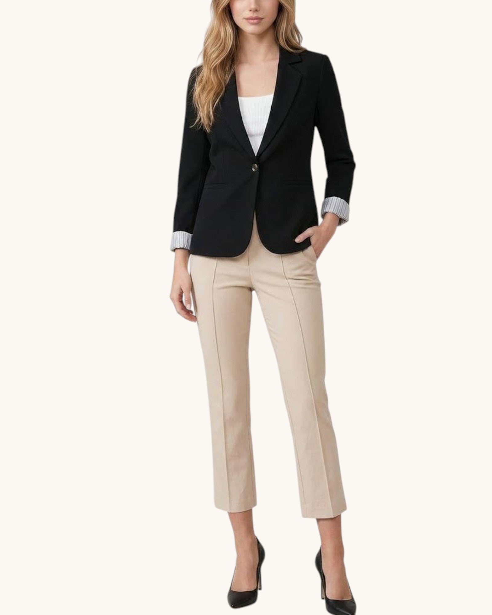 Woman wearing a black blazer and beige pants on a white background.