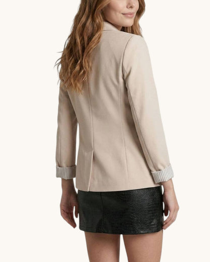 Back view of a woman wearing a beige jacket with striped cuffs on a white background.