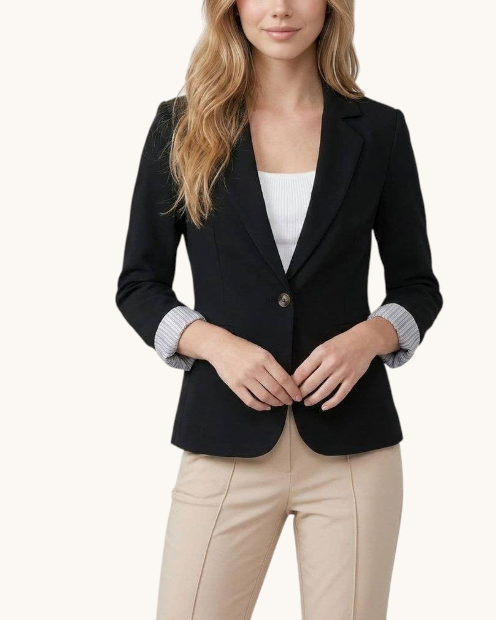 Woman wearing a black blazer over a white top and beige pants on a white background