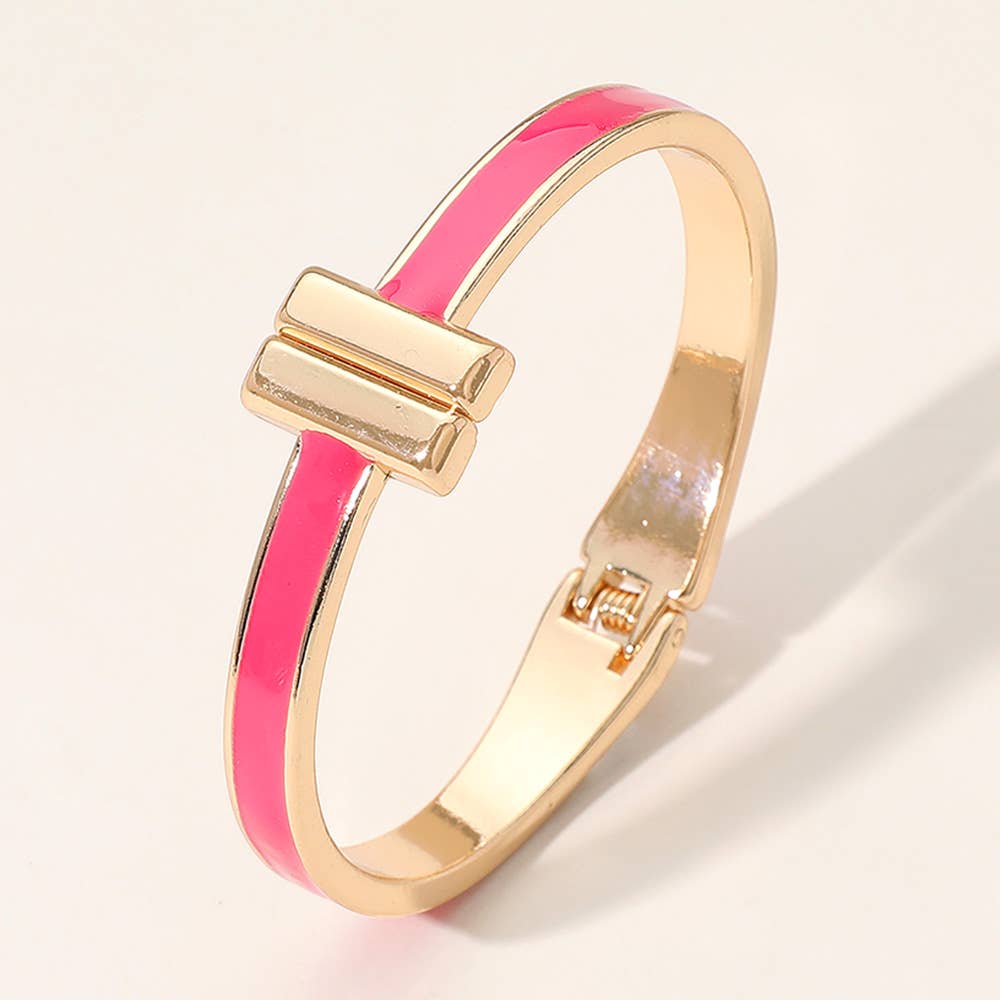 Pink and gold hinge bangle bracelet with T on ends on a light beige background.