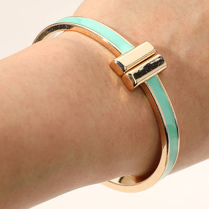 Gold and turquoise metal hinge bangle on a wrist against a neutral background.