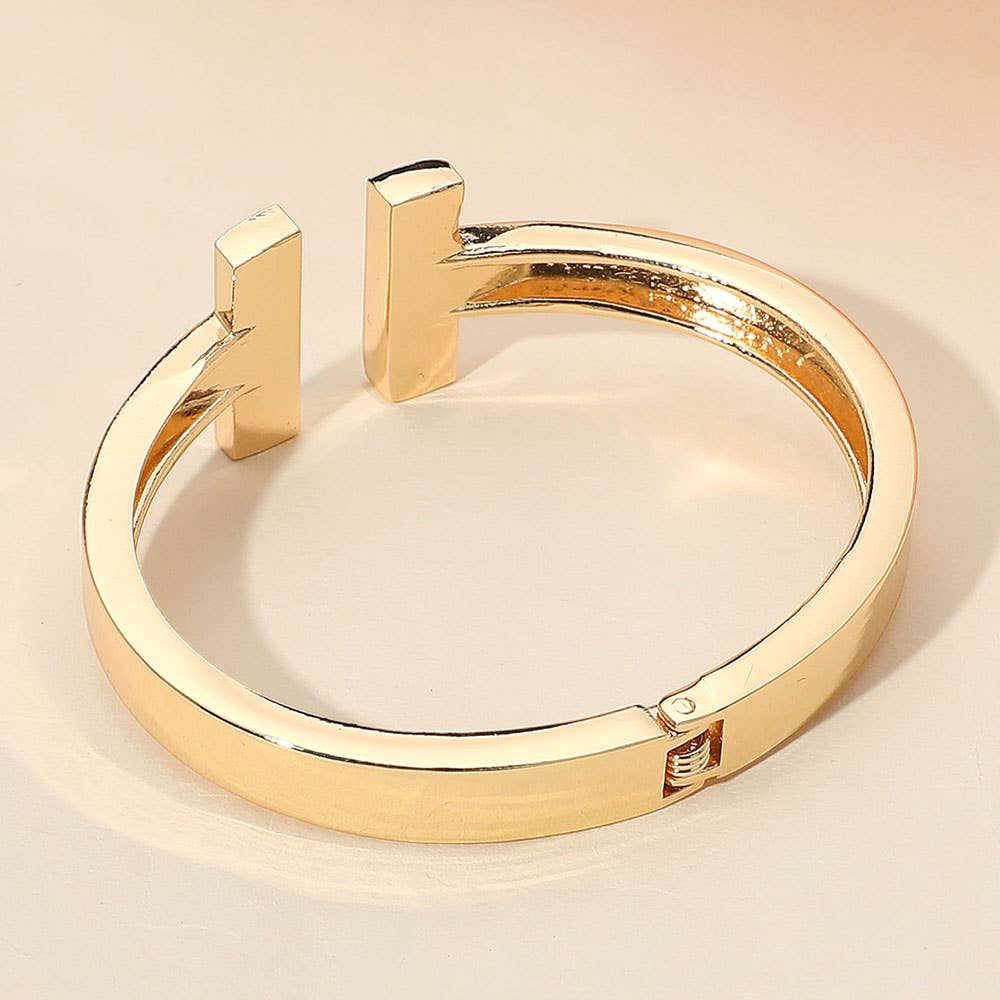 Gold cuff bracelet on a beige background.